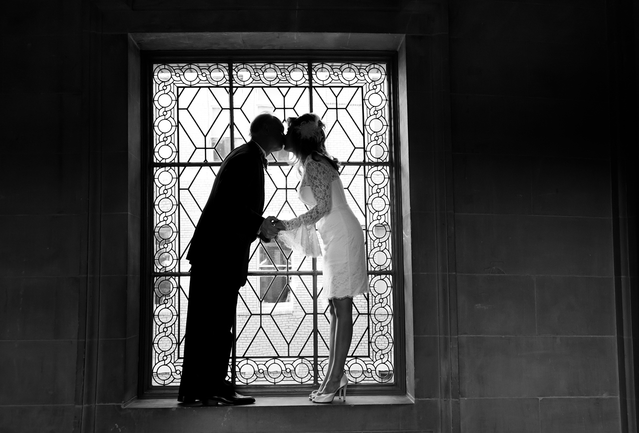 bride and groom kissing in front of window at City Hall